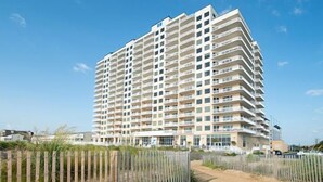 Un hotel de varios pisos con fachada uniforme, situado cerca de una zona arenosa con cerramiento de madera.