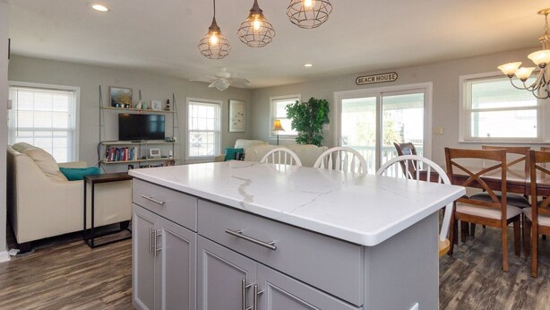 A modern kitchen with a large island, pendant lights, and a dining area with wooden chairs.