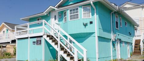 A turquoise two-story house with a white staircase and a small porch.