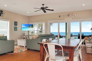 A spacious living room with a wooden dining table, white chairs, a grey sofa, and a television. - ☀️ Gulf Front, Pet Friendly with Elevator | Sailor's Dream ☀️ (Port Saint Joe)