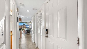 Un pasillo con puertas blancas, una zona de cocina y un comedor con vistas al exterior.