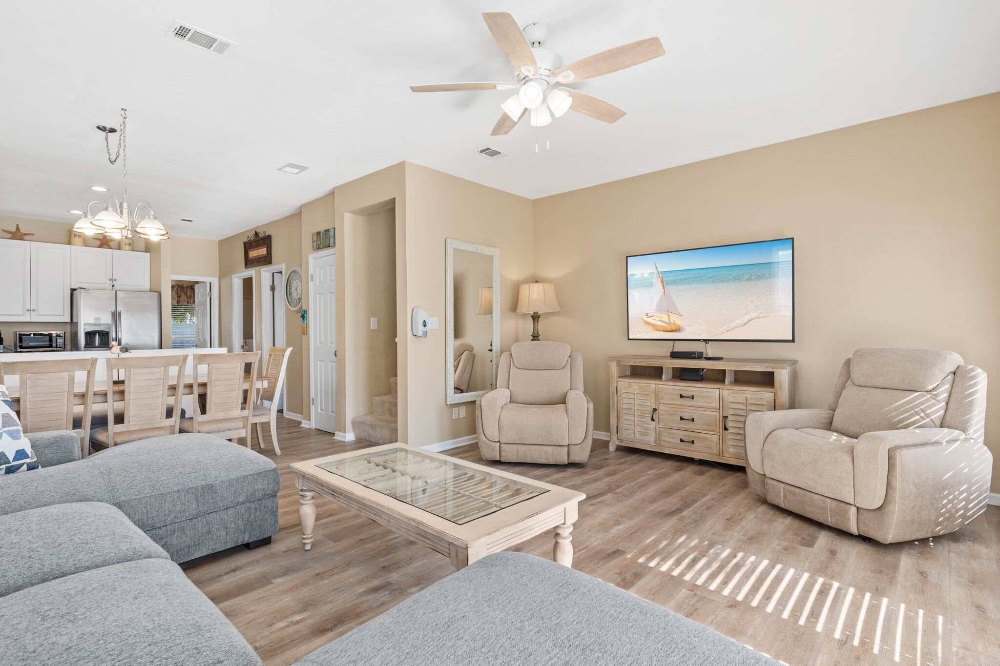 A modern living room with a sofa, armchair, and coffee table. There is a TV mounted on the wall and a ceiling fan.