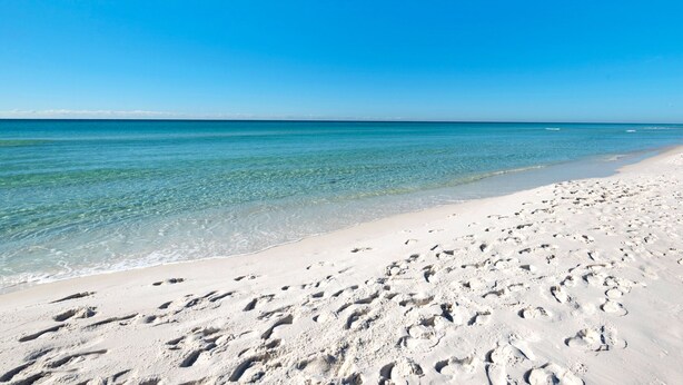 Une plage à l’eau d’un bleu limpide et au sable blanc.