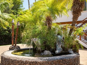 Surrounded by lush tropical plants and palm trees, this serene garden features a circular water feature with a small waterfall.