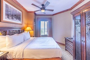 A hotel room with a bed, a ceiling fan, a window with curtains, and a wooden cabinet.