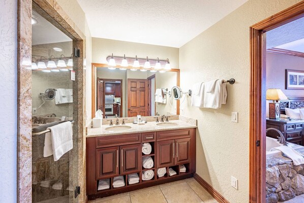 A bathroom with a double sink, vanity, and a large mirror. There are towels hanging on the wall and a towel rack beside the sink.