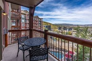 A balcony with a table and chairs, overlooking a pool and buildings.