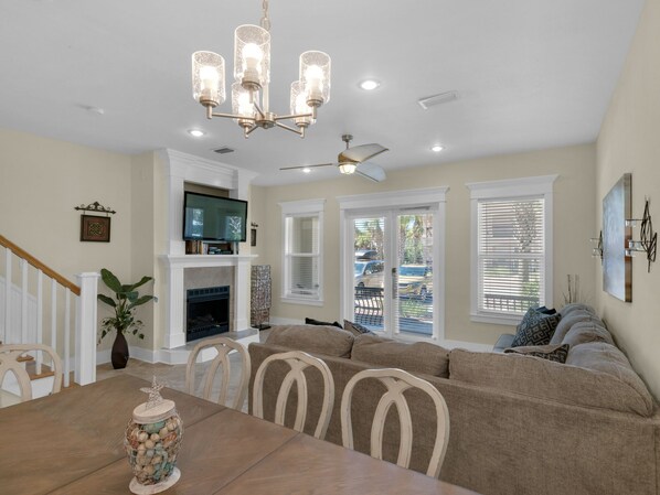 A dining area with a wooden table, chairs, a chandelier, a fireplace, and a television on a mantel.