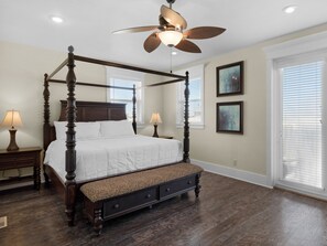 A four-poster bed with a wooden headboard, a bench at the foot of the bed, two bedside tables with lamps, and a ceiling fan.