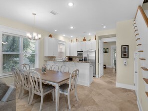 A spacious kitchen with white cabinetry, a central island, and a dining area with a wooden table and chairs. - Spacious Rental-Private Beach Access-Three Story Condo-Close to Pool (Miramar Beach)