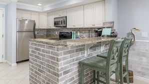 A kitchen with white cabinets, a stainless steel refrigerator, a microwave, and a brick island with bar stools. - Bayfront unit in the popular Makai building (Ocean City)