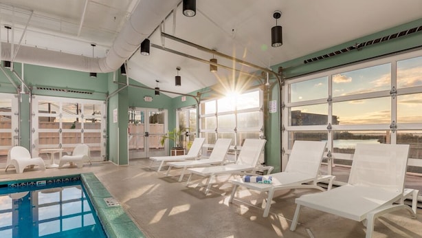 A pool area with sunlit lounge chairs and a clear view of the sunset through large windows. - Bayfront unit in the popular Makai building (Ocean City)