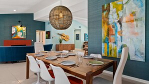 A dining area with a wooden table set for six, white chairs, and a large abstract painting on the wall.