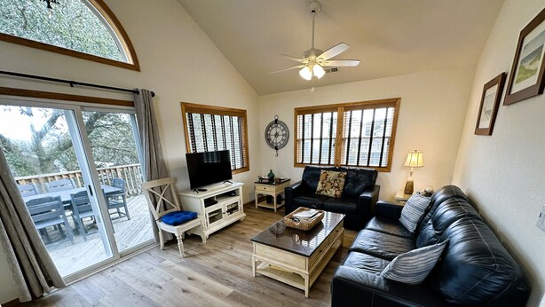 A living room with a wooden floor, a black leather sofa, a white entertainment unit, a dining table, and a large window with blinds. - OS760- Close To Beach, 4BRs, Private Pool, Bubbling Hot Tub and Dog Friendly! (Corolla)