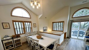 A dining area with a white table and chairs, wooden flooring, and large windows with blinds. - OS760- Close To Beach, 4BRs, Private Pool, Bubbling Hot Tub and Dog Friendly! (Corolla)