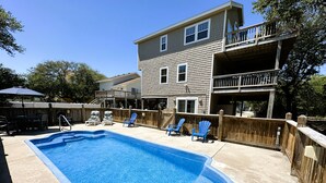 A rectangular swimming pool with a wooden deck, surrounded by a wooden fence, and a two-story house with a balcony in the background. - OS760- Close To Beach, 4BRs, Private Pool, Bubbling Hot Tub and Dog Friendly! (Corolla)