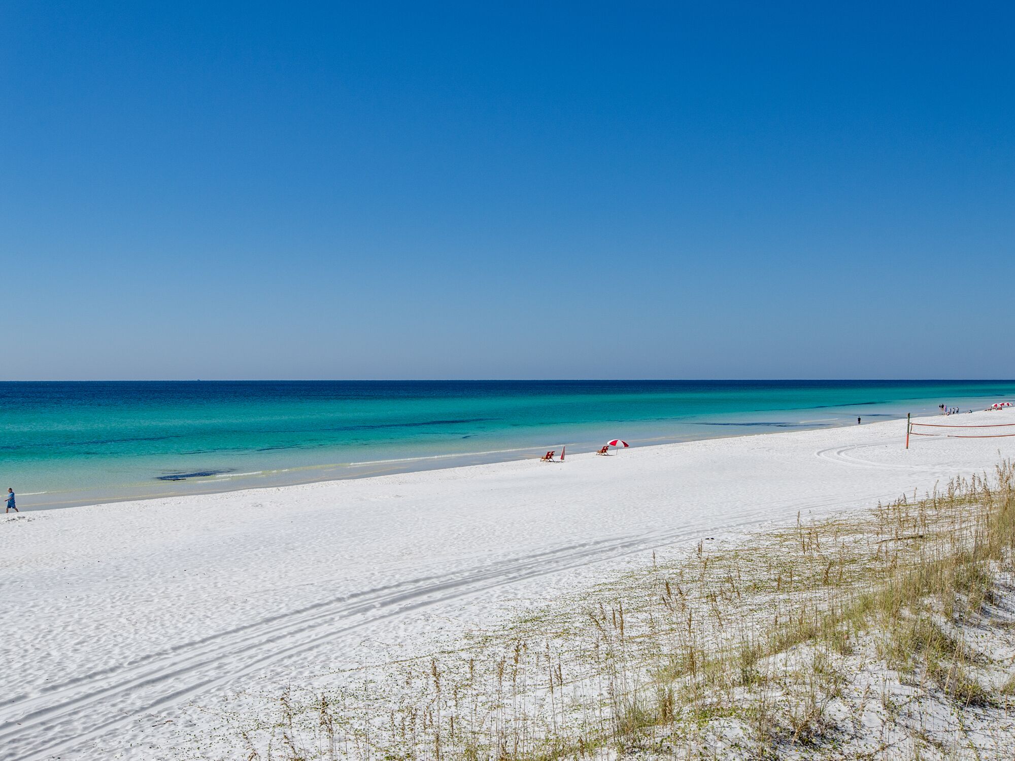 Ein Strand mit weißem Sand, klarem türkisblauem Wasser und einigen Liegestühlen und Sonnenschirmen.