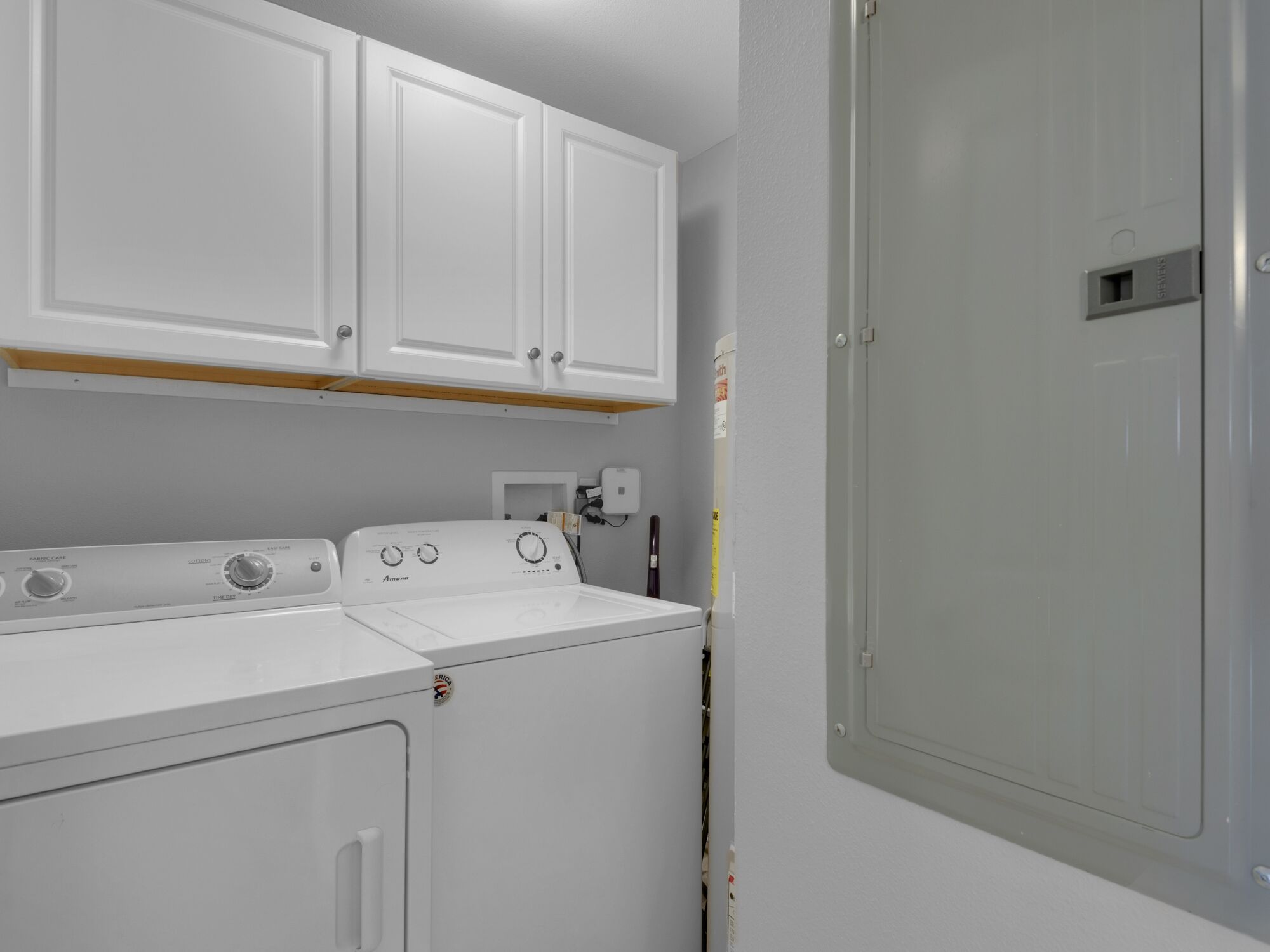 A laundry room with a front-loading washer and dryer, white cabinets above, and a door to the right.