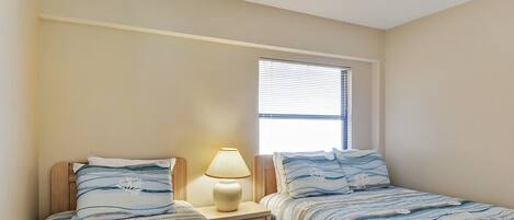 Une chambre avec deux lits simples, une table de chevet avec une lampe et une fenêtre avec des stores.