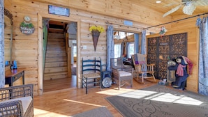 A wooden cabin interior with a staircase, wicker furniture, and a decorative bear figure. - Steps From Lake George! 8-Acre Home w/ Dock Access (Ticonderoga)