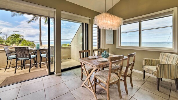 Un comedor con una mesa y sillas de madera, una lámpara colgante y ventanas amplias con vista al océano.