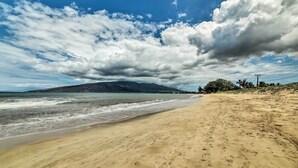 Una playa con arena, una montaña al fondo y un cielo parcialmente nublado.