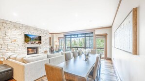 Un salón amplio con chimenea de piedra, un televisor grande montado en la pared y un comedor con una mesa larga y sillas.