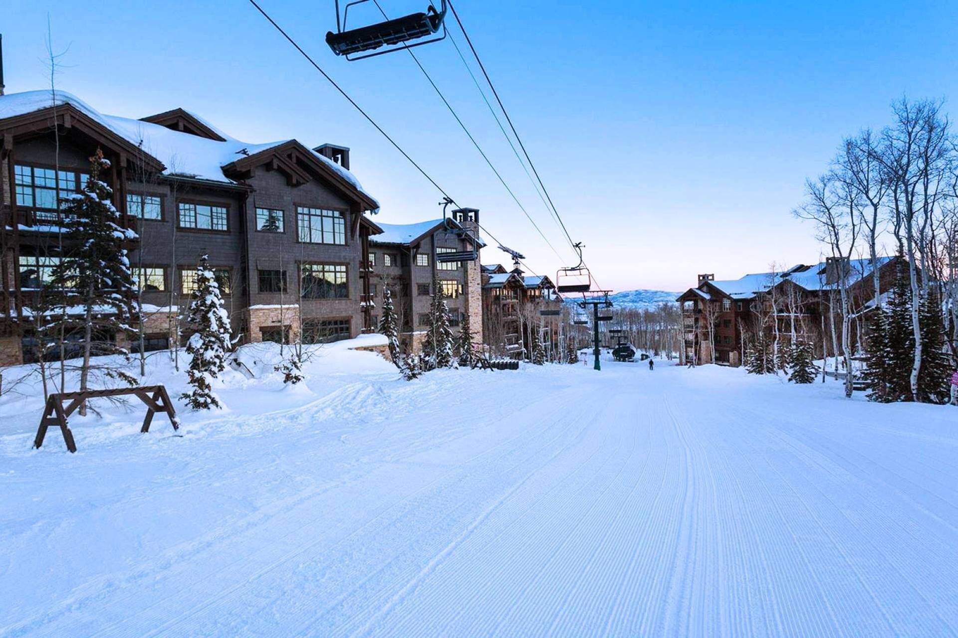 Une station de ski enneigée, avec de grands bâtiments en bois, des remontées mécaniques et un ciel dégagé.
