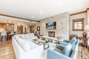 A spacious living area with a stone fireplace, a kitchen in the background, and a dining area with bar stools.