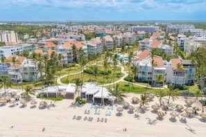Un complexe hôtelier comprenant plusieurs bâtiments, des palmiers et une plage aménagée avec des chaises longues.
