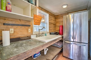 A kitchen with a stainless steel refrigerator, wooden walls, a white sink, and a window with blinds. - Guadalupe Riverfront Studio w/ Private Balcony (Seguin)