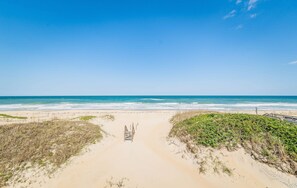 Camí de platja que condueix a l'oceà, amb una passera de fusta i dunes herboses.