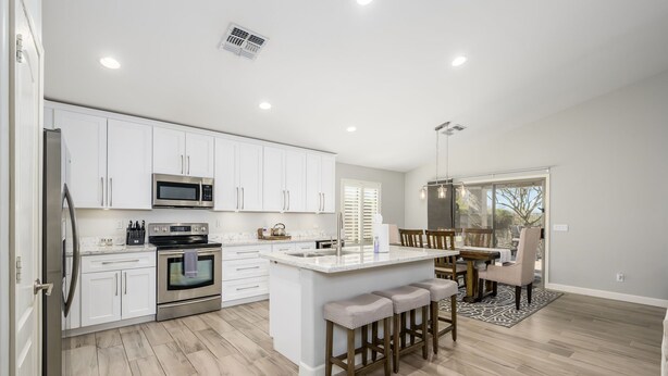 A modern kitchen with white cabinetry, stainless steel appliances, and a central island with bar stools. - Cave Creek Beauty with Sunset and Golf Course Views! (Cave Creek)