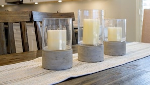 A kitchen with white cabinets, a wooden table, and three candles in glass holders. - Cave Creek Beauty with Sunset and Golf Course Views! (Cave Creek)