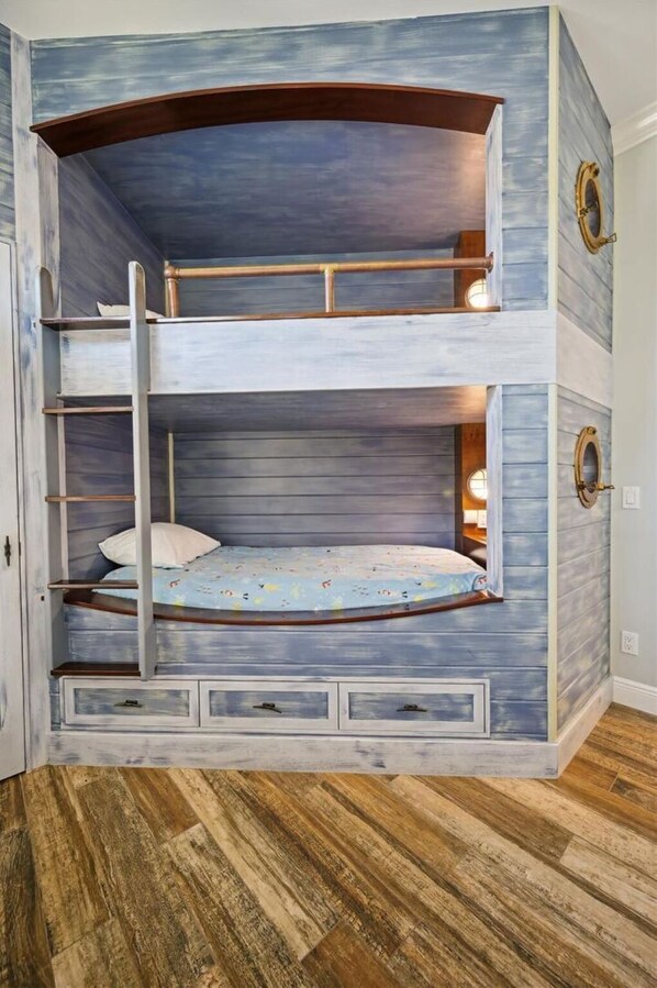 Una cama litera con escritorio integrado y cajones, suelo de madera y diseño rústico.