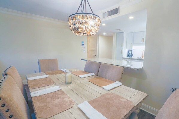 Un comedor con mesa de madera, sillas acolchadas y una araña.
