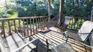 A wooden deck with outdoor furniture, including chairs and a table with a plate of food and a cup.
