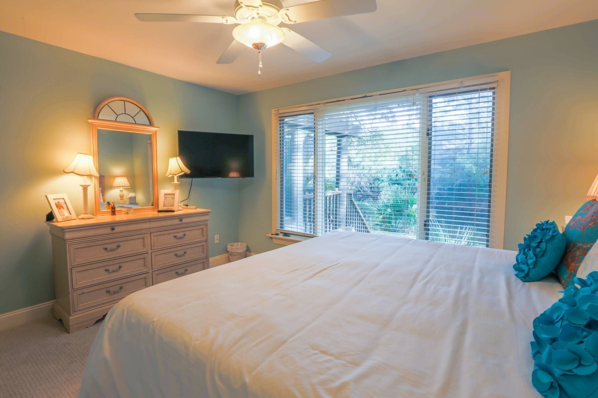 Un dormitorio con cama, cómoda, televisor y ventilador de techo.
