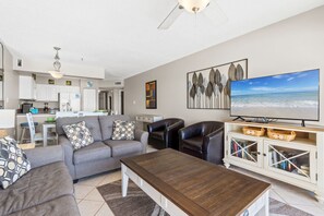 A living room with a sofa, coffee table, TV, and a dining area with chairs and a table.