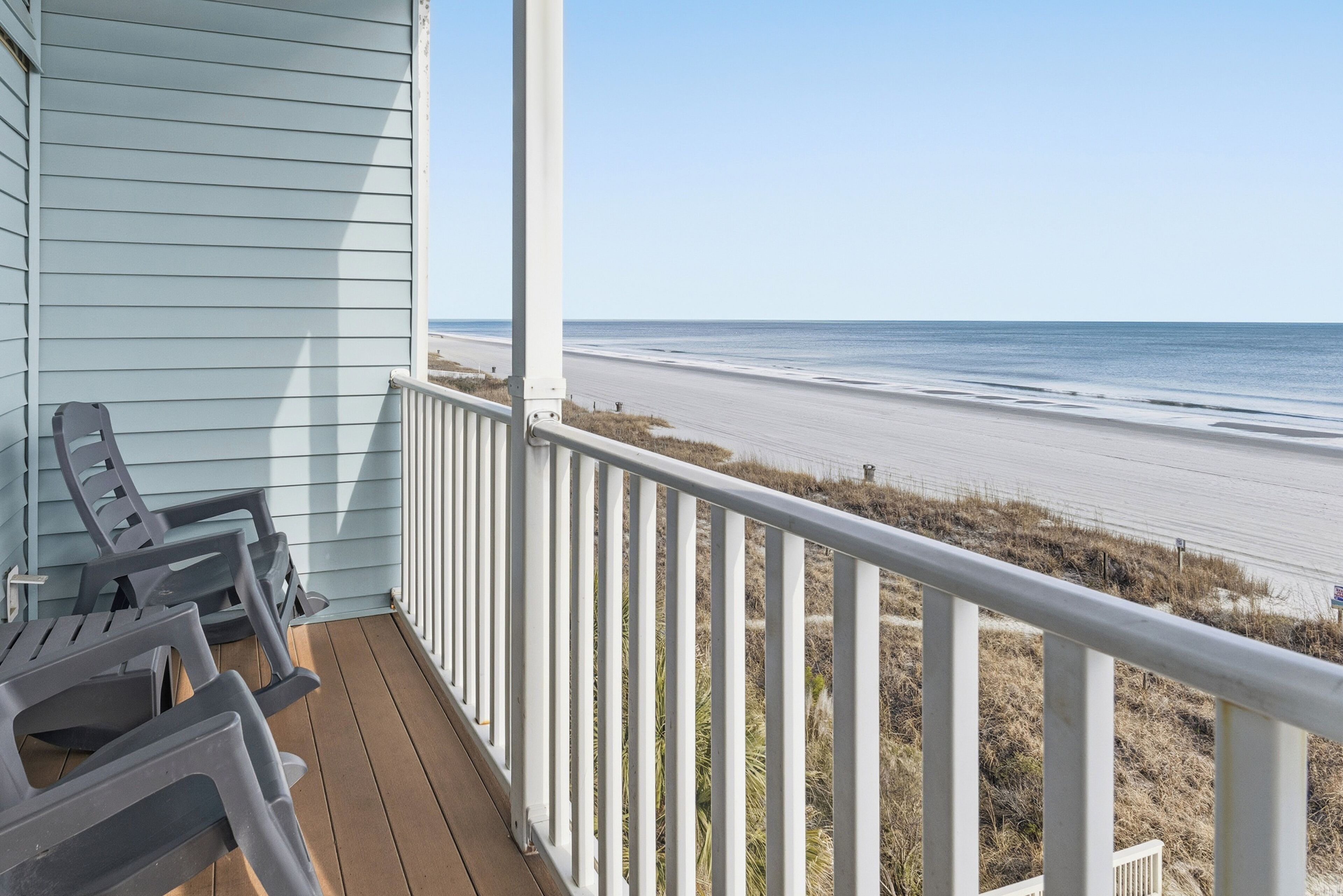 Een houten terras met stoelen, met uitzicht op het strand.