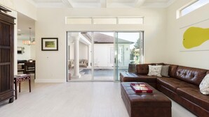 Ein geräumiges Wohnzimmer mit einer braunen Ledersofa, einem Holztisch und einer Glasschiebetür, die zu einem Außenbereich führt.