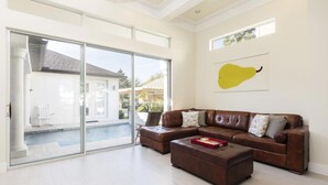 Ein großzügiges Wohnzimmer mit einem braunen Leder-Sofa, einem Couchtisch und einer Glastür zu einem Poolbereich.