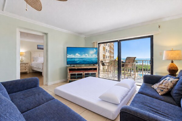 A hotel room with a bed, a TV, a balcony with chairs, and a view of the ocean.