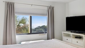 A bedroom with a bed, a television on a white cabinet, and a window with curtains. - Ultimate Beach Getaway | 3BR Direct Oceanfront Condo w/ Stunning Balcony Views! 🌴 (Cape Canaveral)