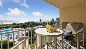 A balcony with a pool view, a bottle, and a hat on a table. - Ultimate Beach Getaway | 3BR Direct Oceanfront Condo w/ Stunning Balcony Views! 🌴 (Cape Canaveral)