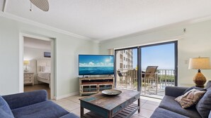 A living room with a sofa, a coffee table, and a TV. There is a balcony with a view of the sea. - Ultimate Beach Getaway | 3BR Direct Oceanfront Condo w/ Stunning Balcony Views! 🌴 (Cape Canaveral)