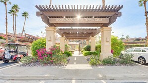 Una entrada techada al Santa Rosa Swim & Tennis Club, con un pérgola, palmeras y un camino que conduce a la entrada.