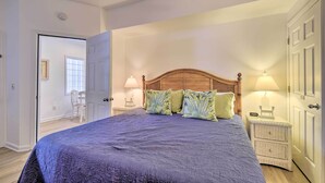 A bedroom with a large bed, wooden headboard, two bedside tables with lamps, and a door leading to another room. - Sunset Beach Retreat - Monthly Rentals Welcome! (Sunset Beach)