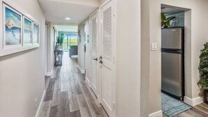 Un couloir avec un plancher en bois, des murs blancs et un réfrigérateur dans la partie cuisine.