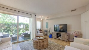 Un salon spacieux doté d’un grand téléviseur, de sièges confortables et d’une porte-fenêtre coulissante donnant sur un balcon.